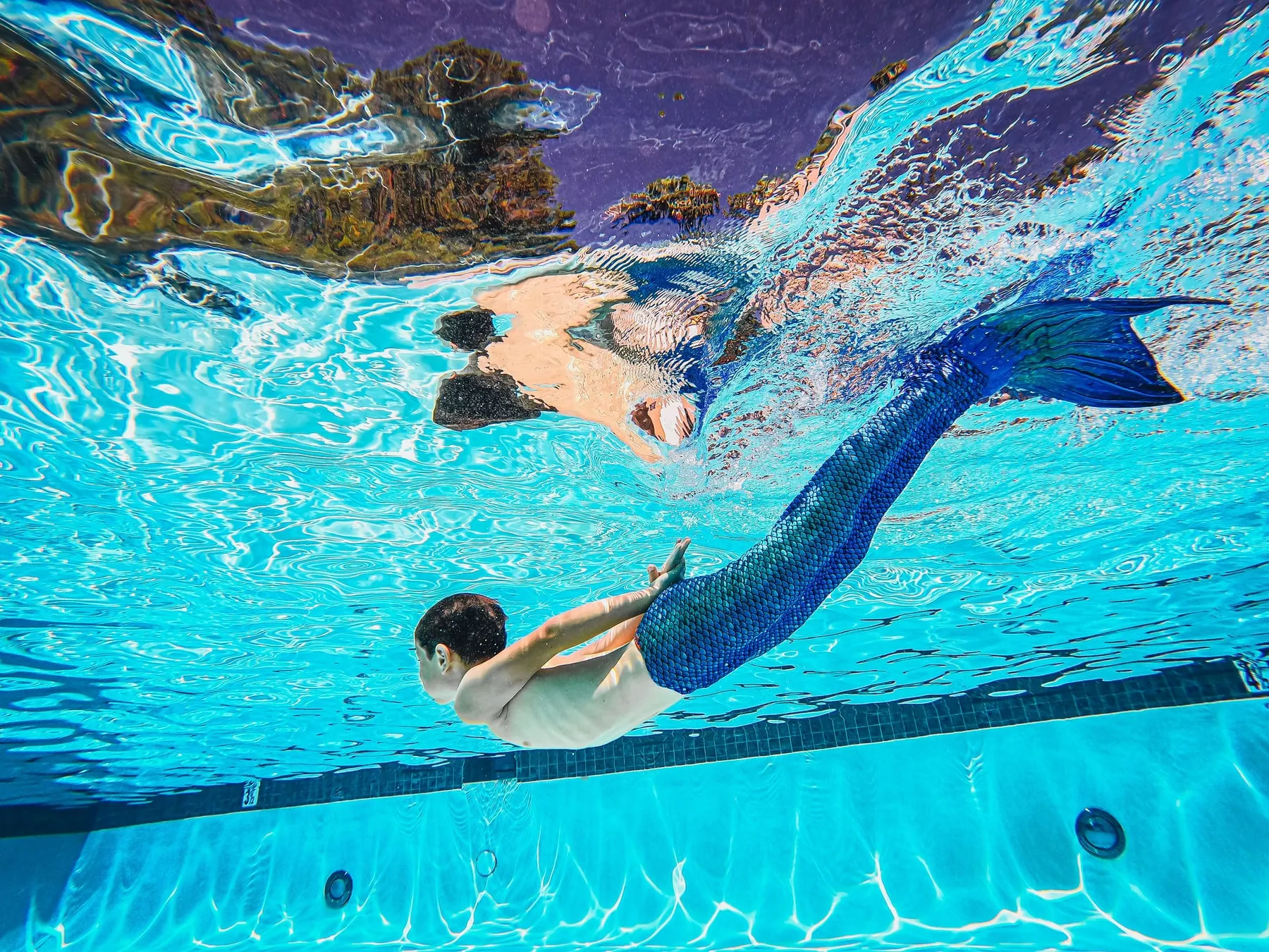 Kind dat onder water met een blauwe zeemeerminstaart zwemt